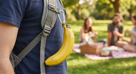 Yellow banana-shaped steel flask clipped to a backpack strap