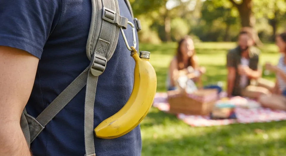 Yellow banana-shaped steel flask clipped to a backpack strap