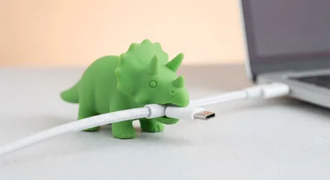 Green rubber dinosaur protecting a white charging cable